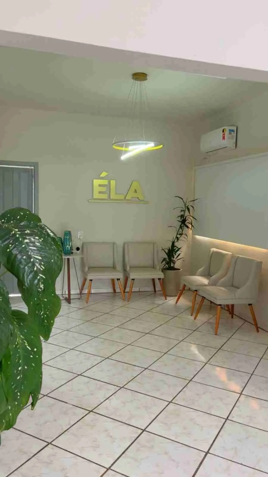 Recepção da Clínica ÉLA, com cadeiras claras, plantas e luminária circular