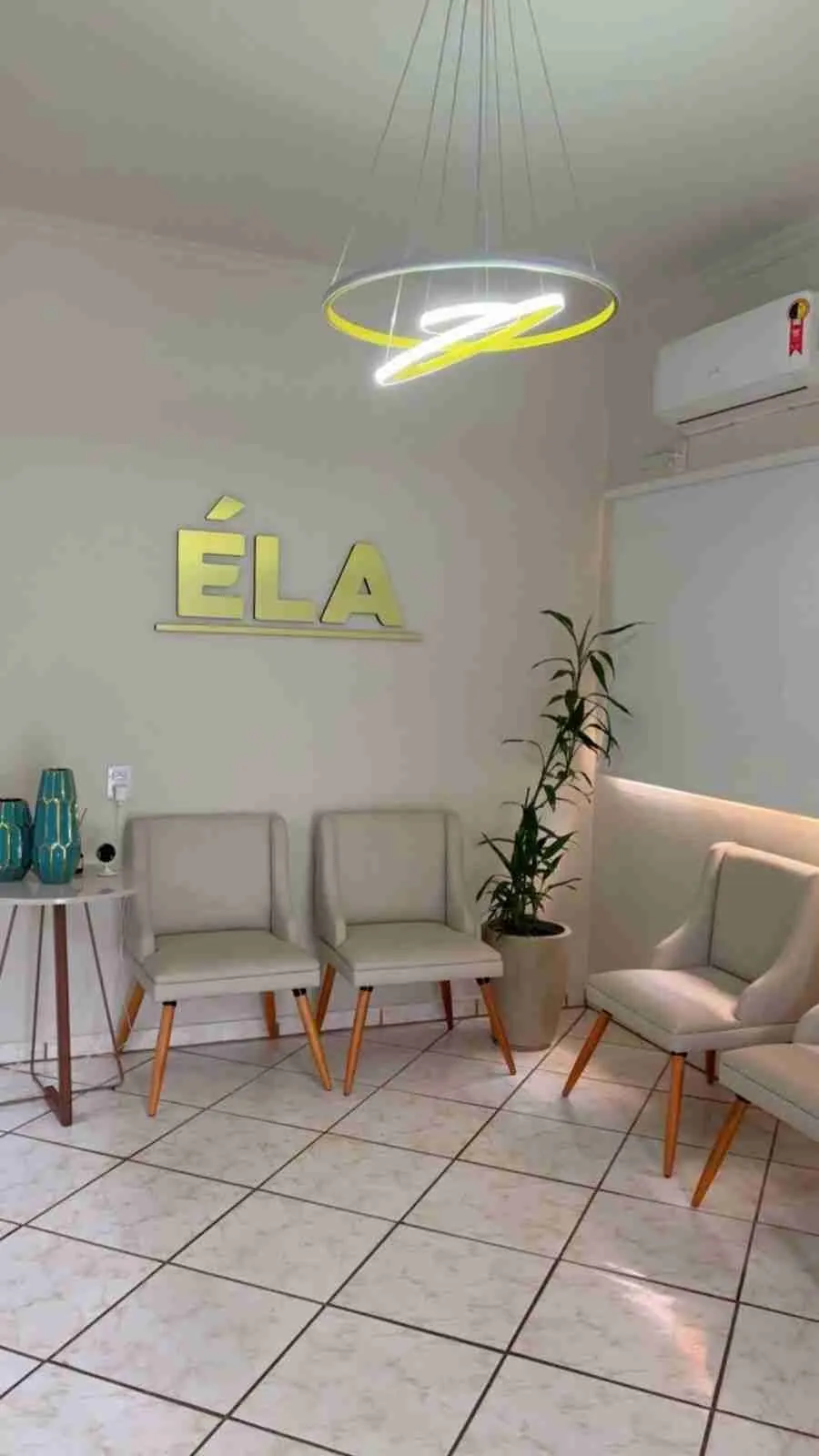 Sala de espera da Clínica ÉLA, com poltronas claras e o letreiro dourado ÉLA na parede